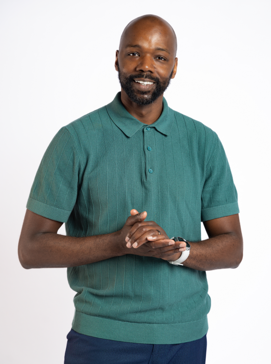 A smiling man with a beard and a bald head wearing a green polo shirt, standing against a white background.