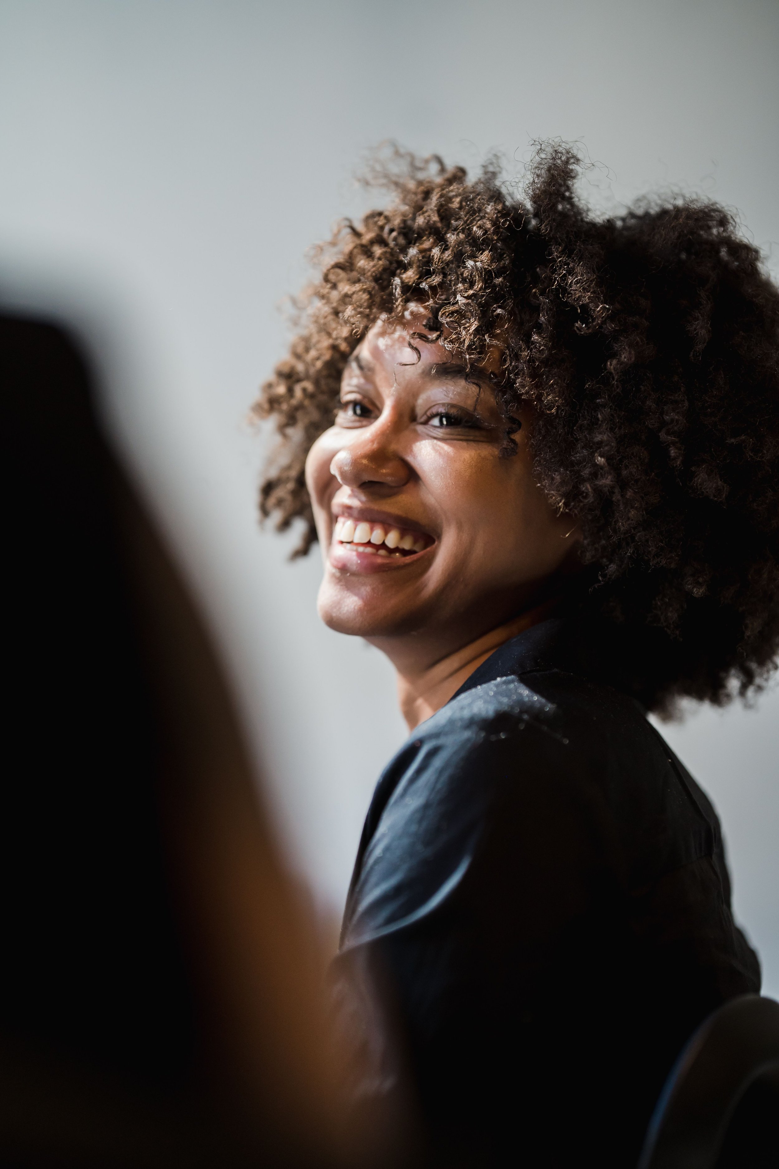 Close-up of a woman with dark, curly hair smiling and looking to her left.