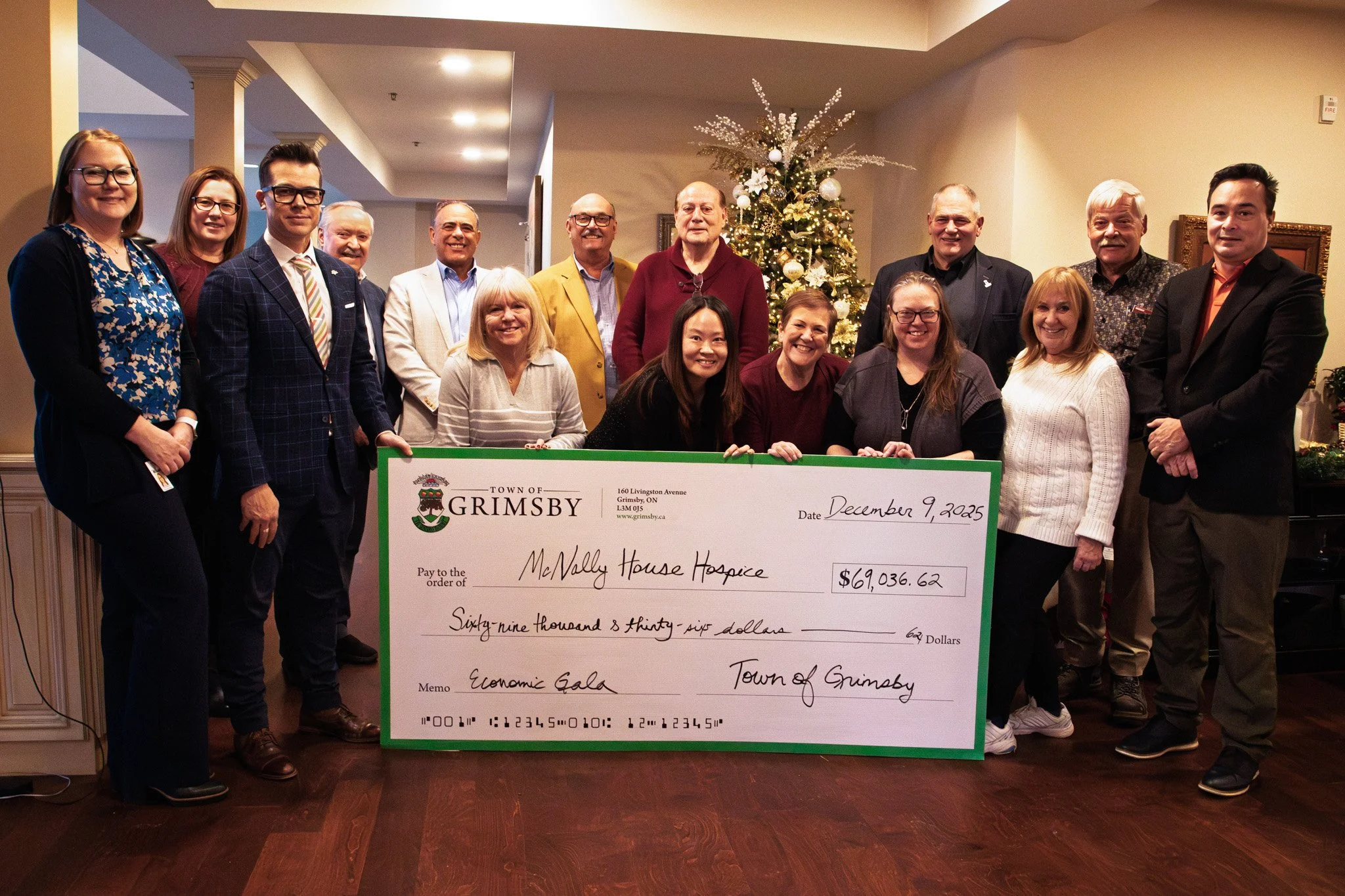 Group of people standing in front of a decorated Christmas tree, holding a large check for $69,036.62 made out to McNally House Hospice, at an event called the Economic Gala in the Town of Grimsby, on December 9, 2025.