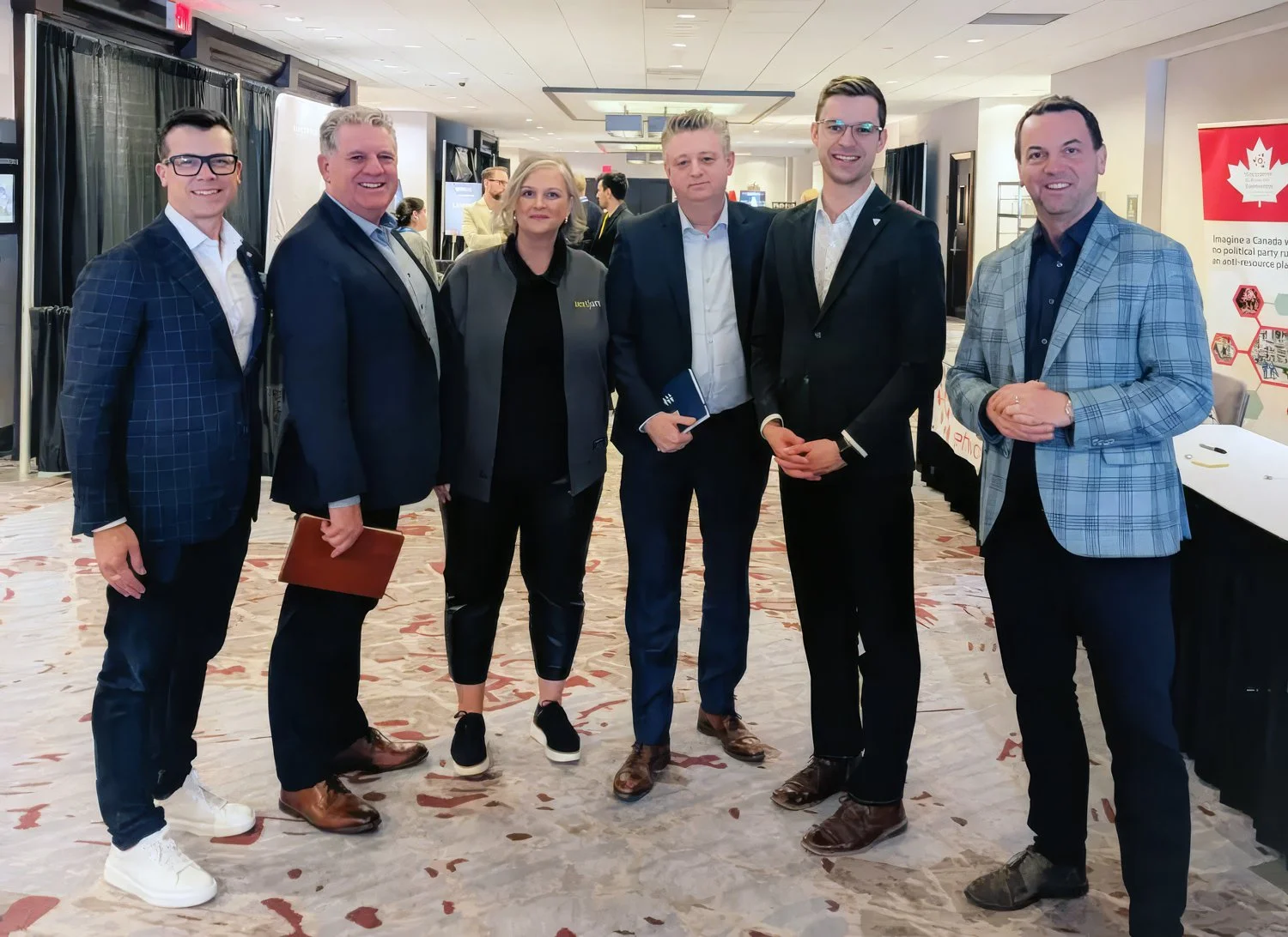 Group of seven professionally dressed people standing together at a business or conference event in an indoor venue.