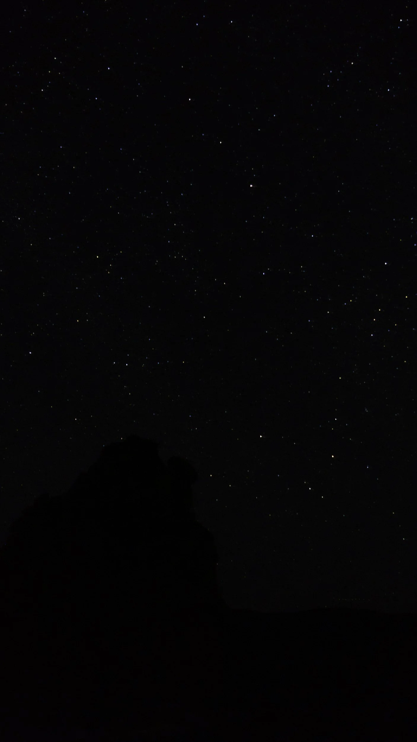 Night sky filled with numerous stars, with dark silhouettes of mountains at the bottom.