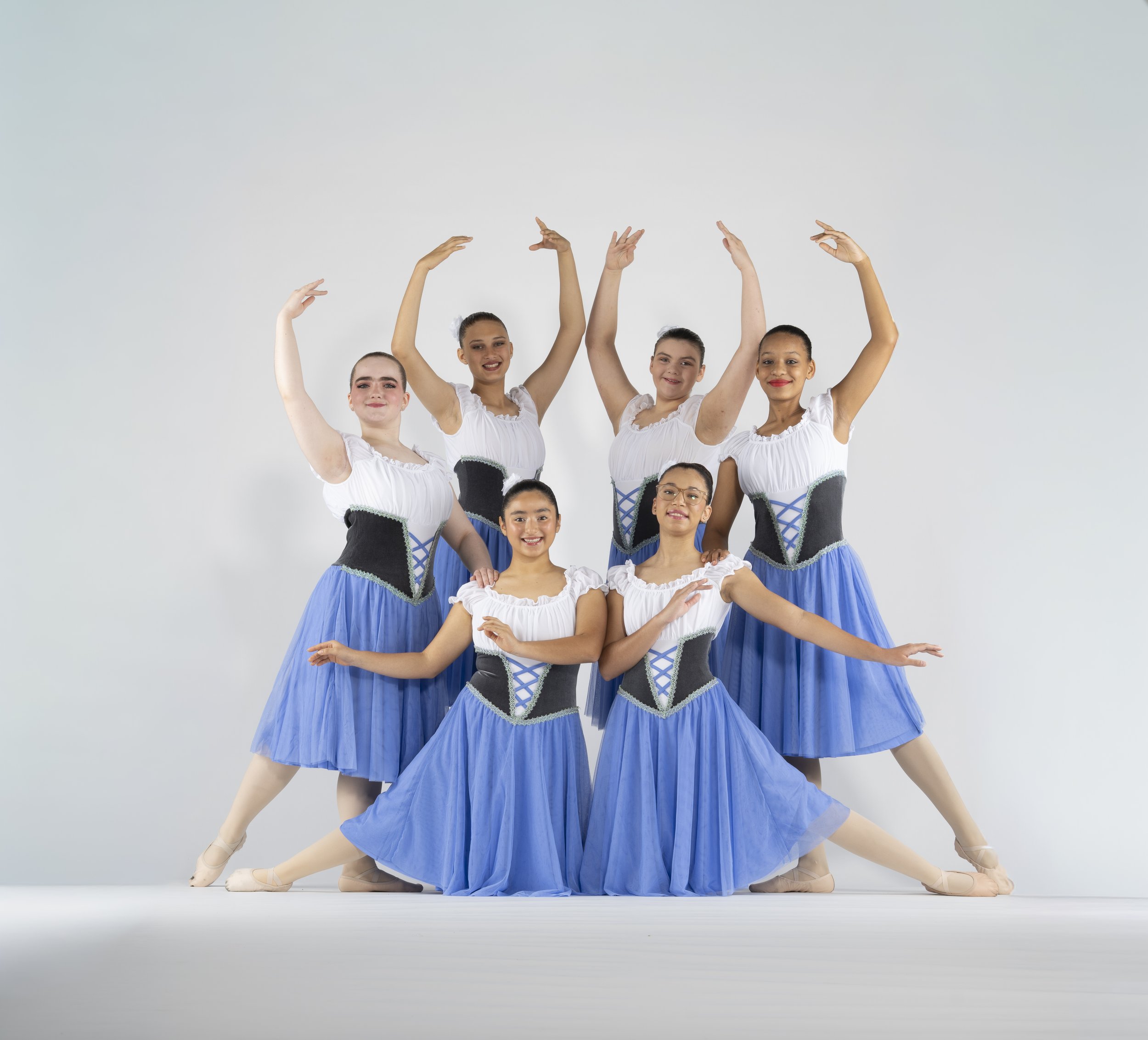 A group of ballerinas in blue and white costumes performing a ballet pose against a plain background.