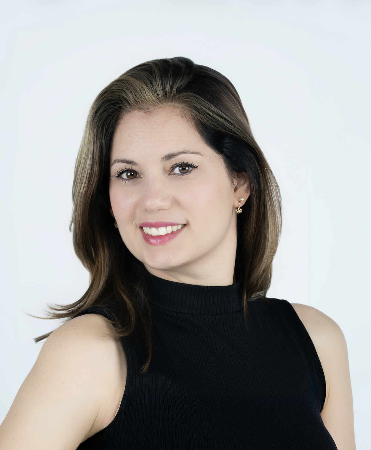 A young woman with brown hair styled with blonde highlights, smiling and wearing a black sleeveless turtleneck, with a plain white background.