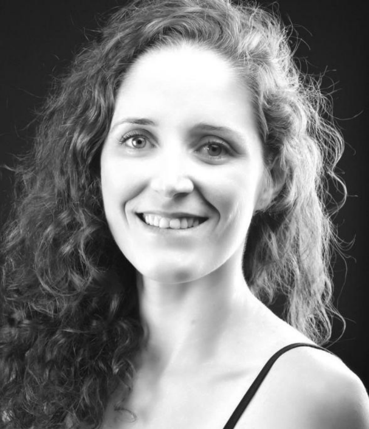 A smiling woman with curly hair in a black and white portrait.