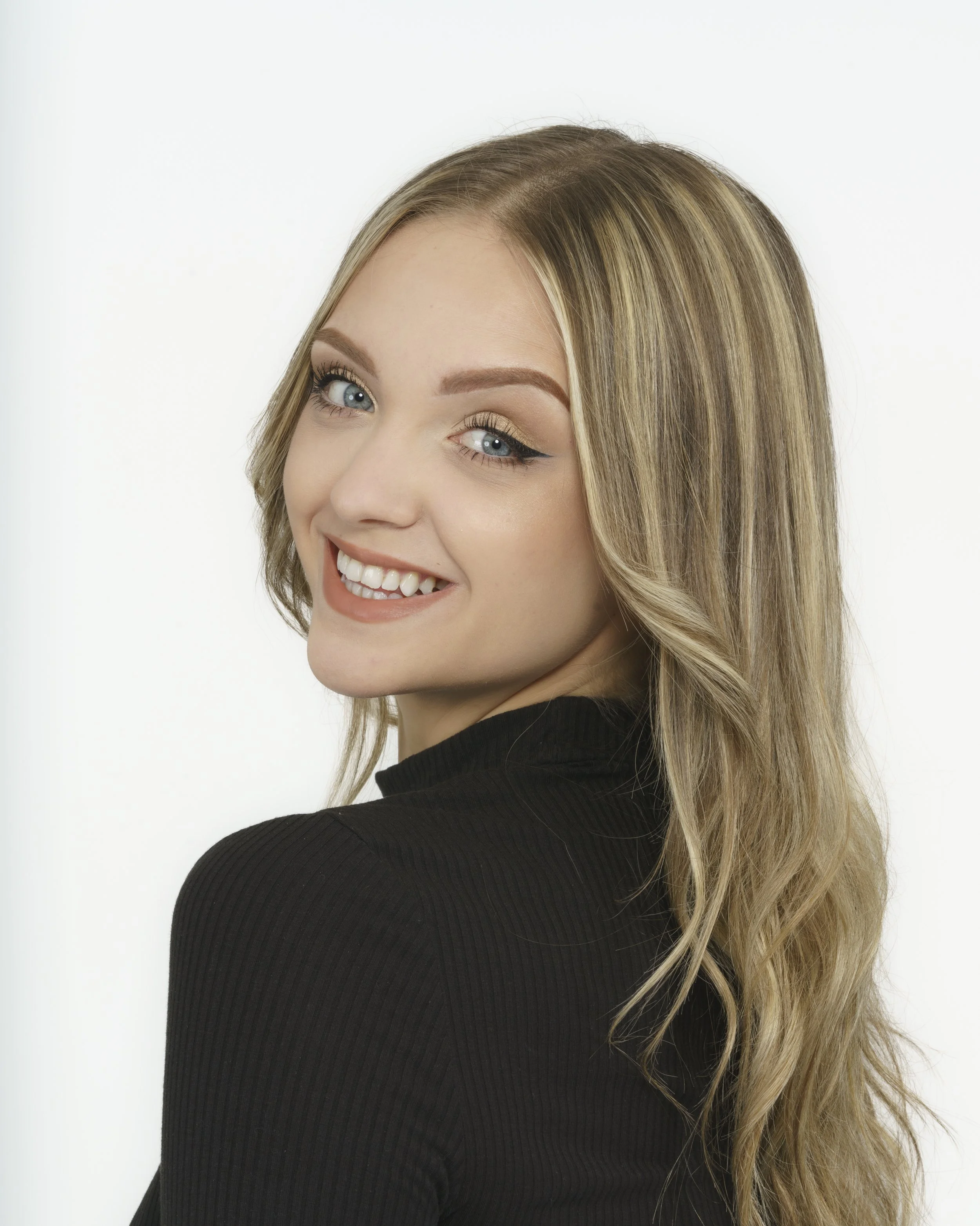 Close-up of a woman with blonde hair and blue eyes smiling, wearing a black top, against a white background.