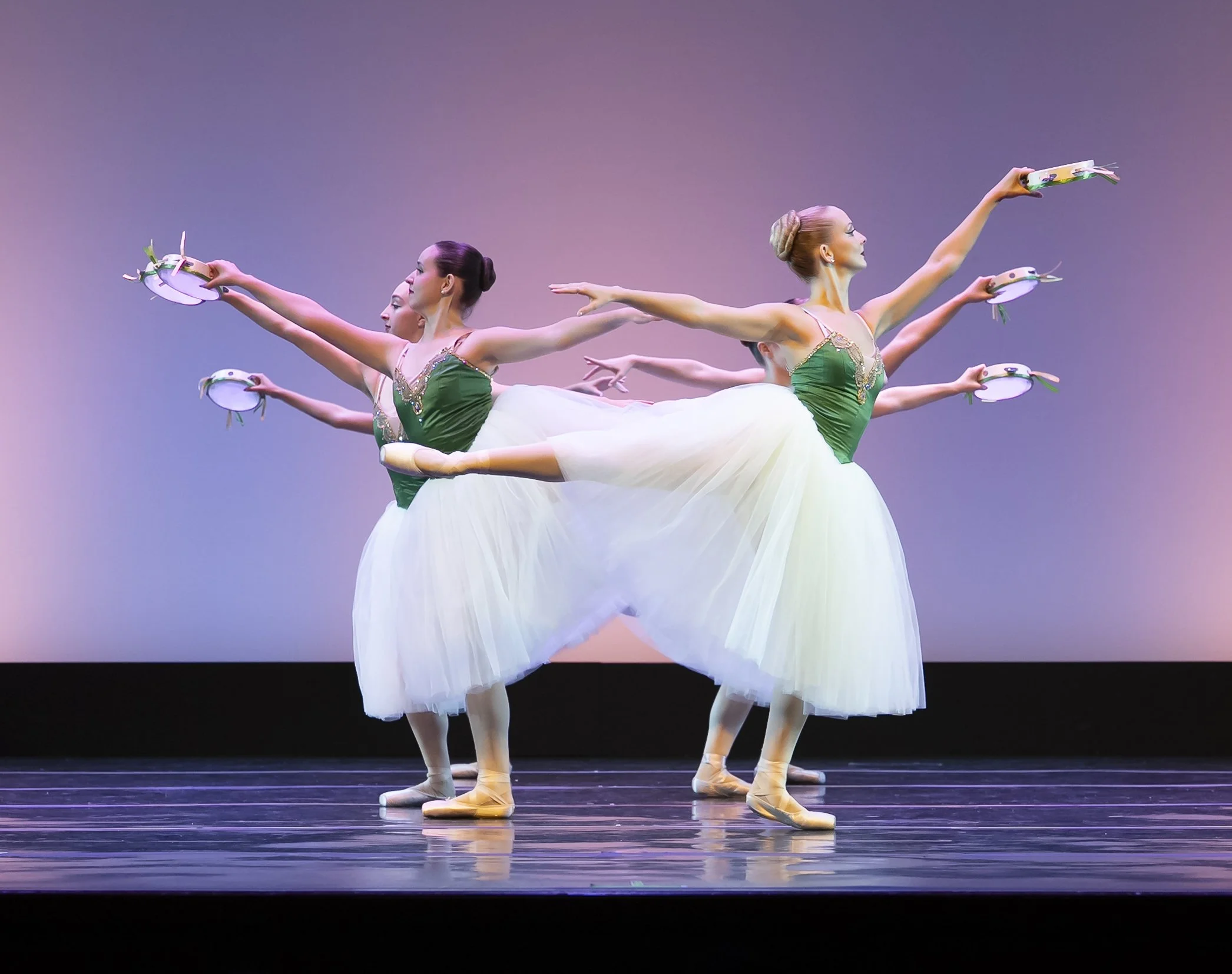 Ballet dancers in green costumes performing on stage with pink and purple gradient background.