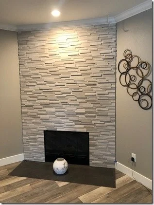 Modern living room with a white textured stone fireplace, round metal wall art, and a white decorative vase on the dark hearth.