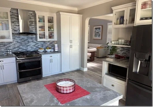 Modern kitchen with white cabinets, gray backsplash, stainless steel stove, black refrigerator, and kitchen island with a basket on a red placemat.