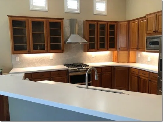 Kitchen with wooden cabinets, a white countertop, a stainless steel stove with a vent hood, and small windows above.