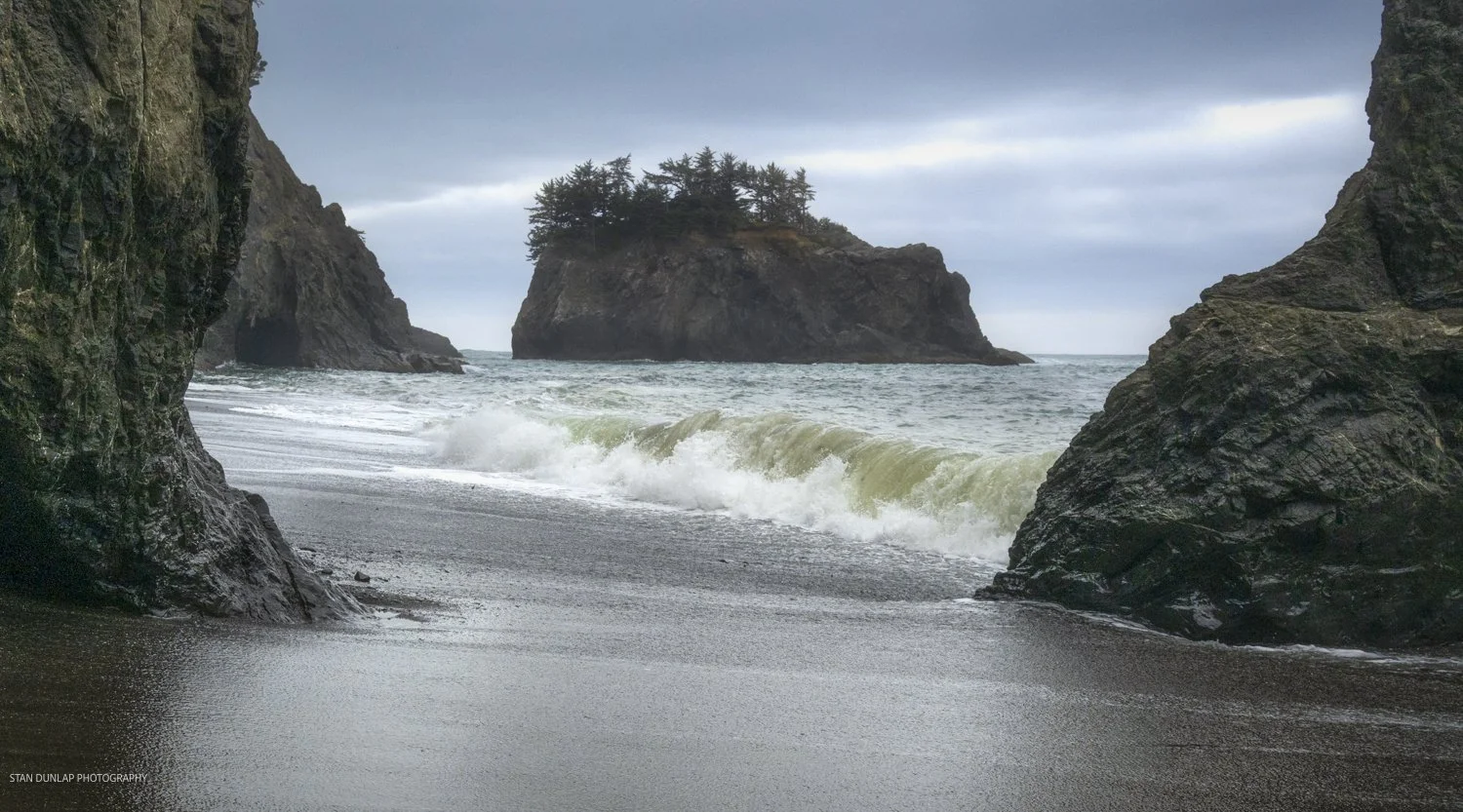 Rugged cliffs along the Oregon coast framing a sea stack on a windy, overcast day.