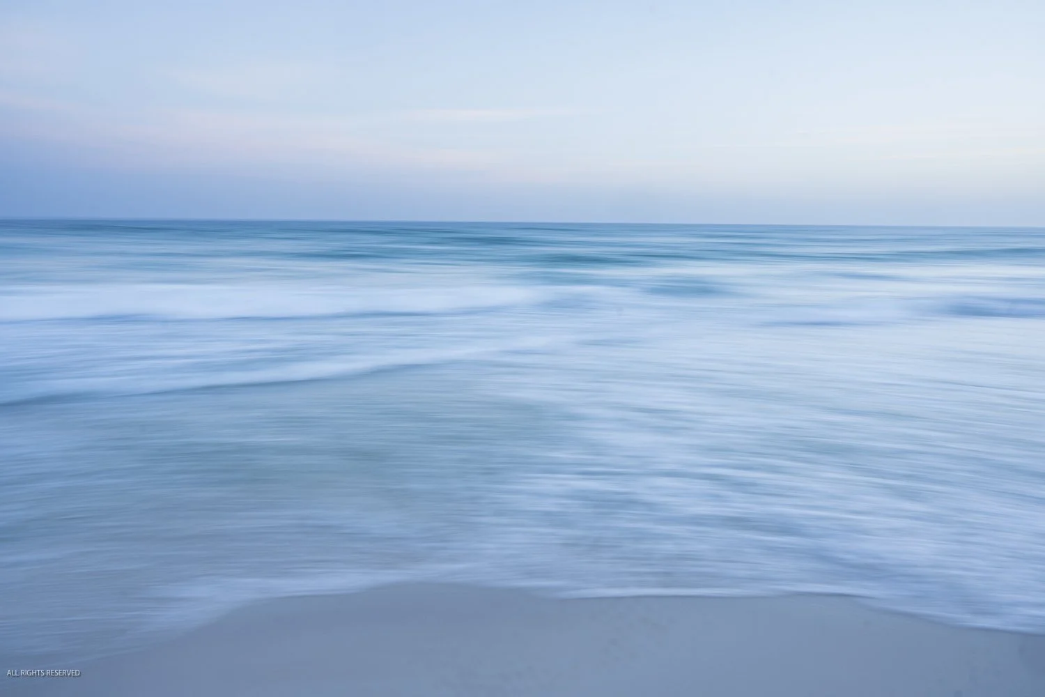 Soft blue waves rolling onto the Alabama coast beneath a calm evening sky.