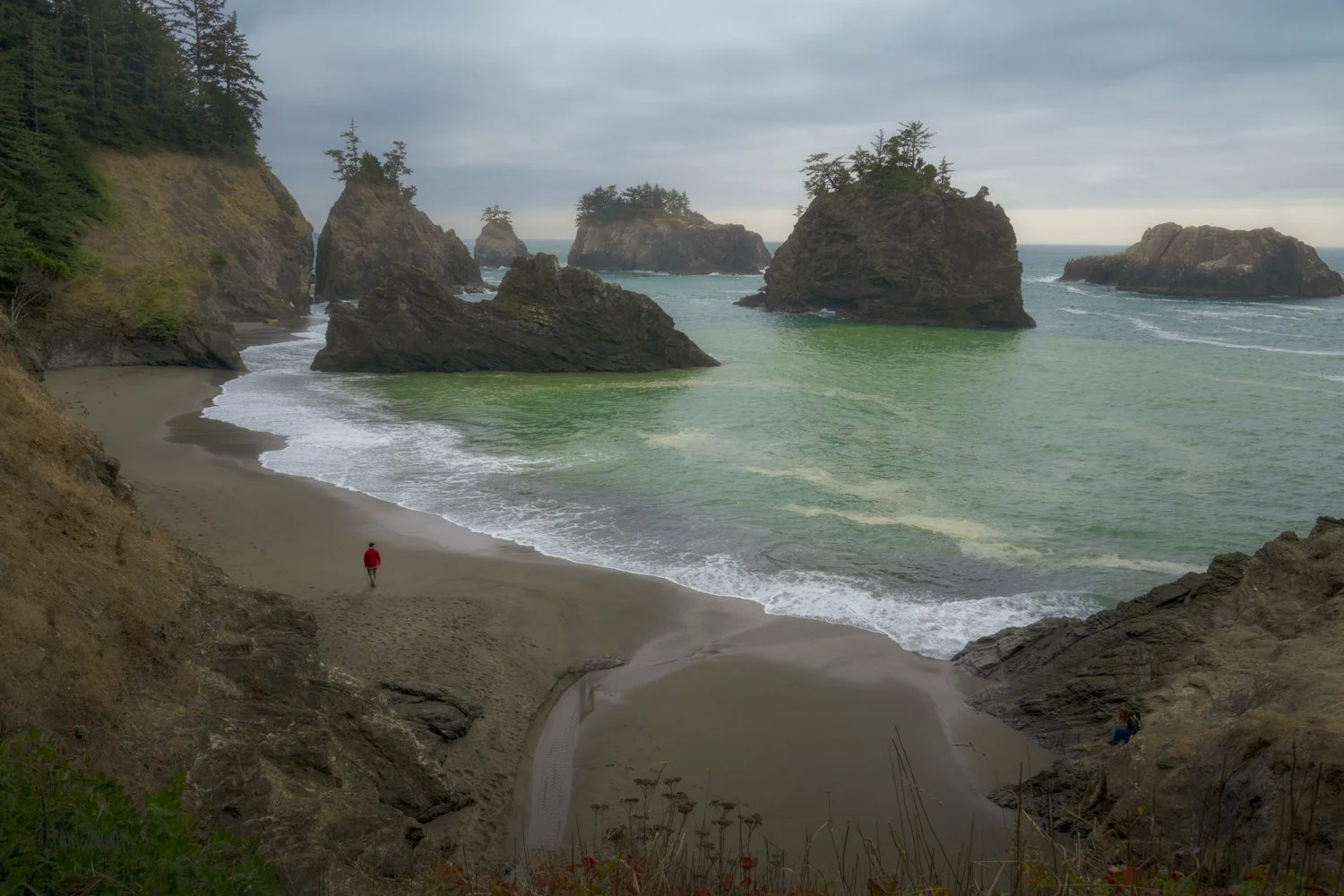 A photo of Stan walking down a beach of sea stacks on Oregon's Secret Beach with sea stacks