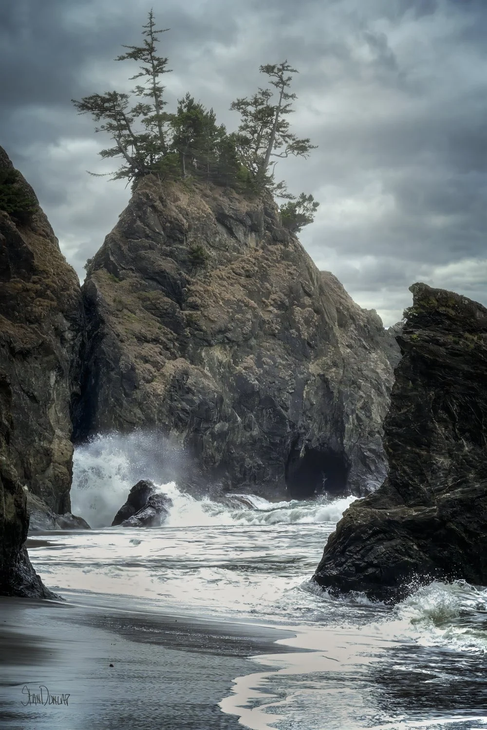 A sea stack being hit by waves under a stormy sky on the Oregon coastline