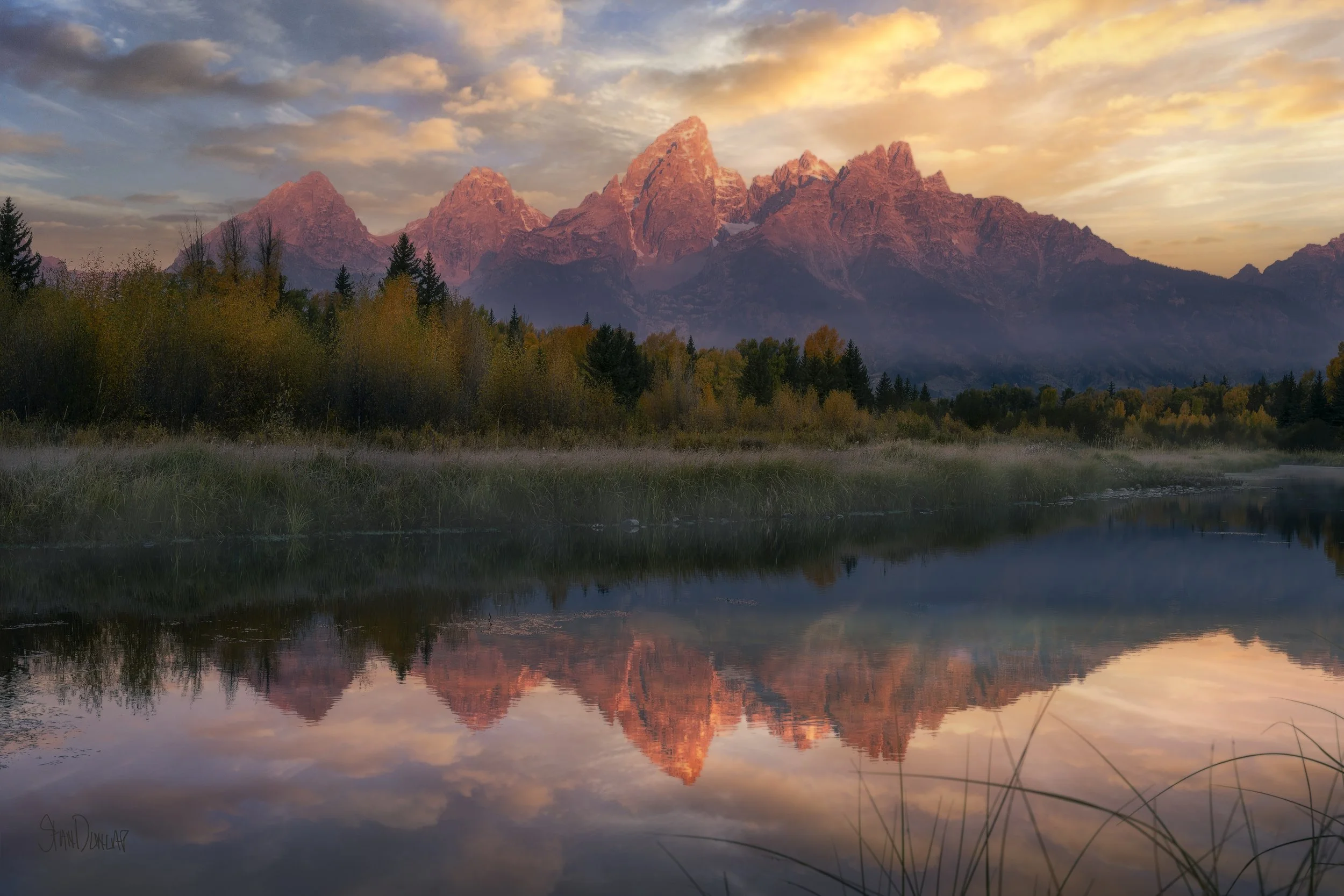 The Teton Mountains under clouds at sunrise reflecting in the snake river in fall