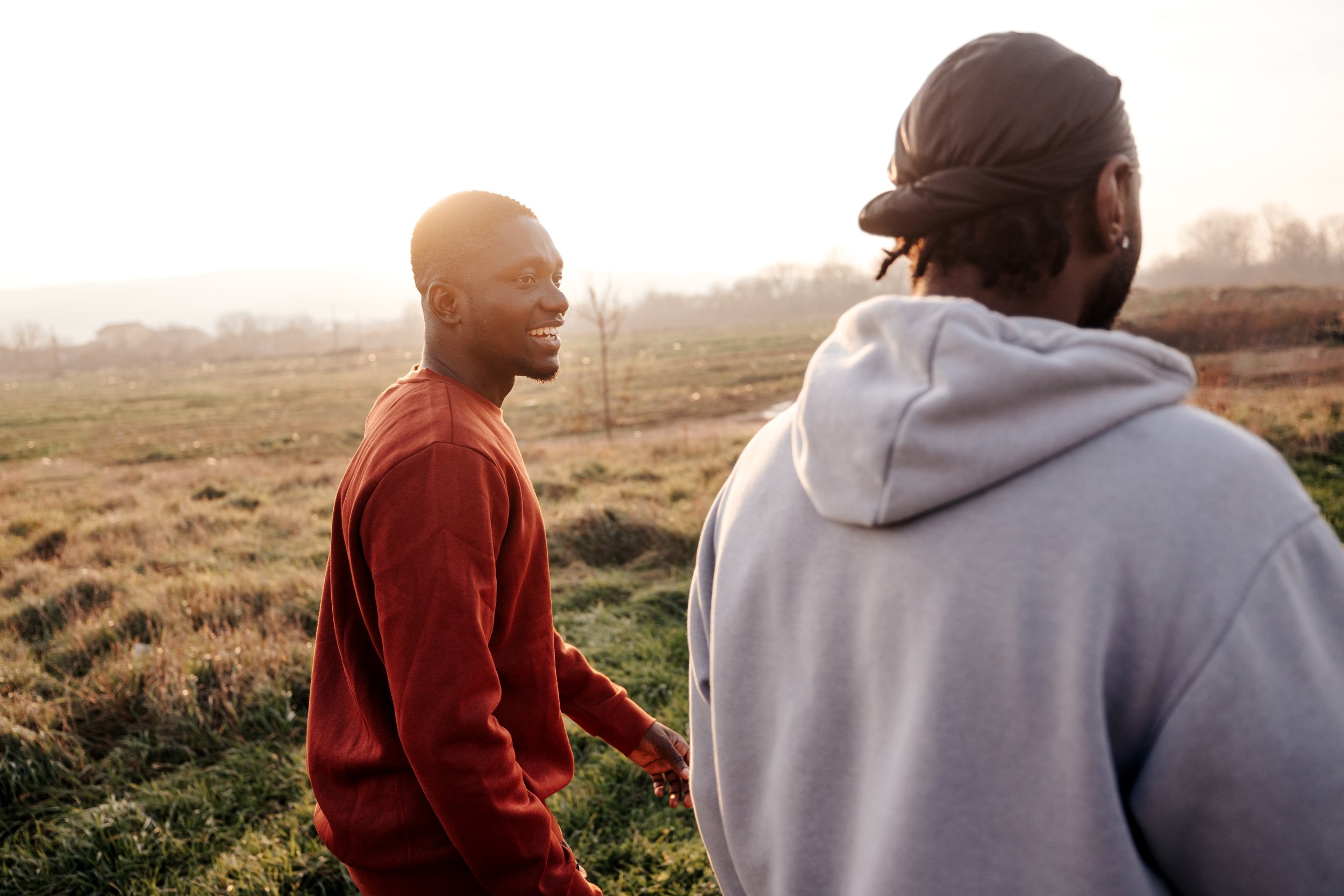 Two young men holding hands outdoors during sunset, smiling and interacting with each other in a rural landscape.