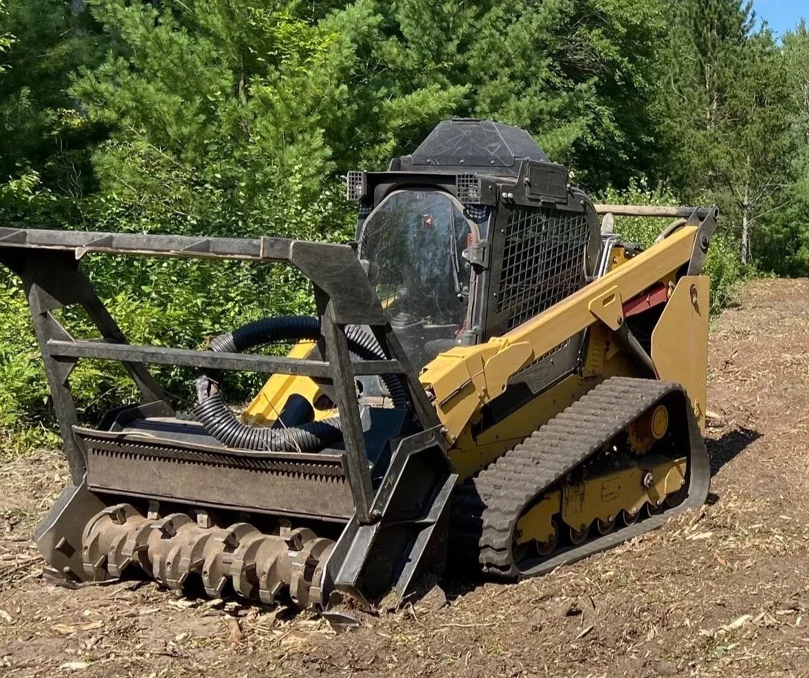 Small bulldozer working on a dirt path with green trees and blue sky in the background.