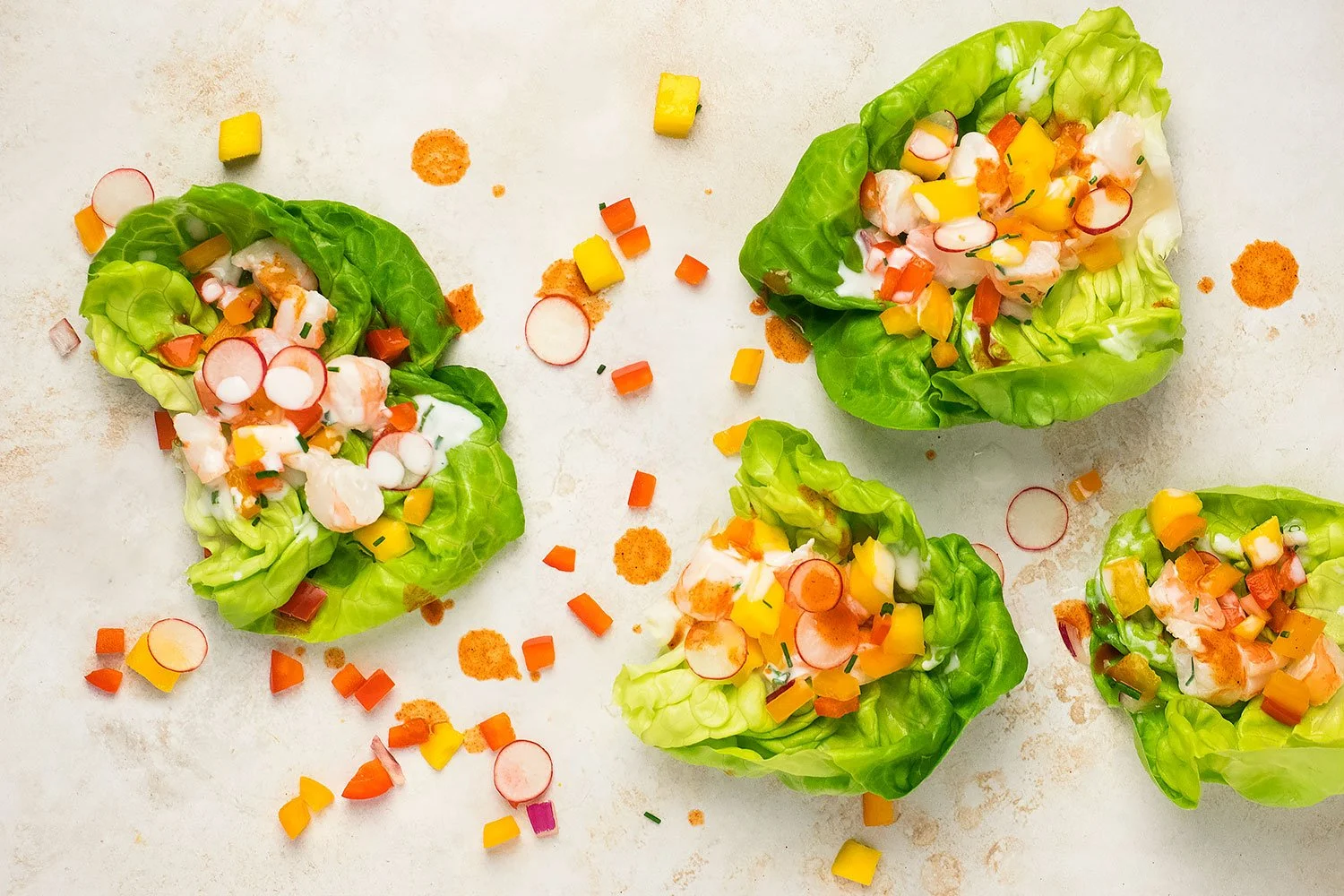 Overhead view of lettuce cups filled with shrimp, diced bell peppers, radishes, and creamy dressing