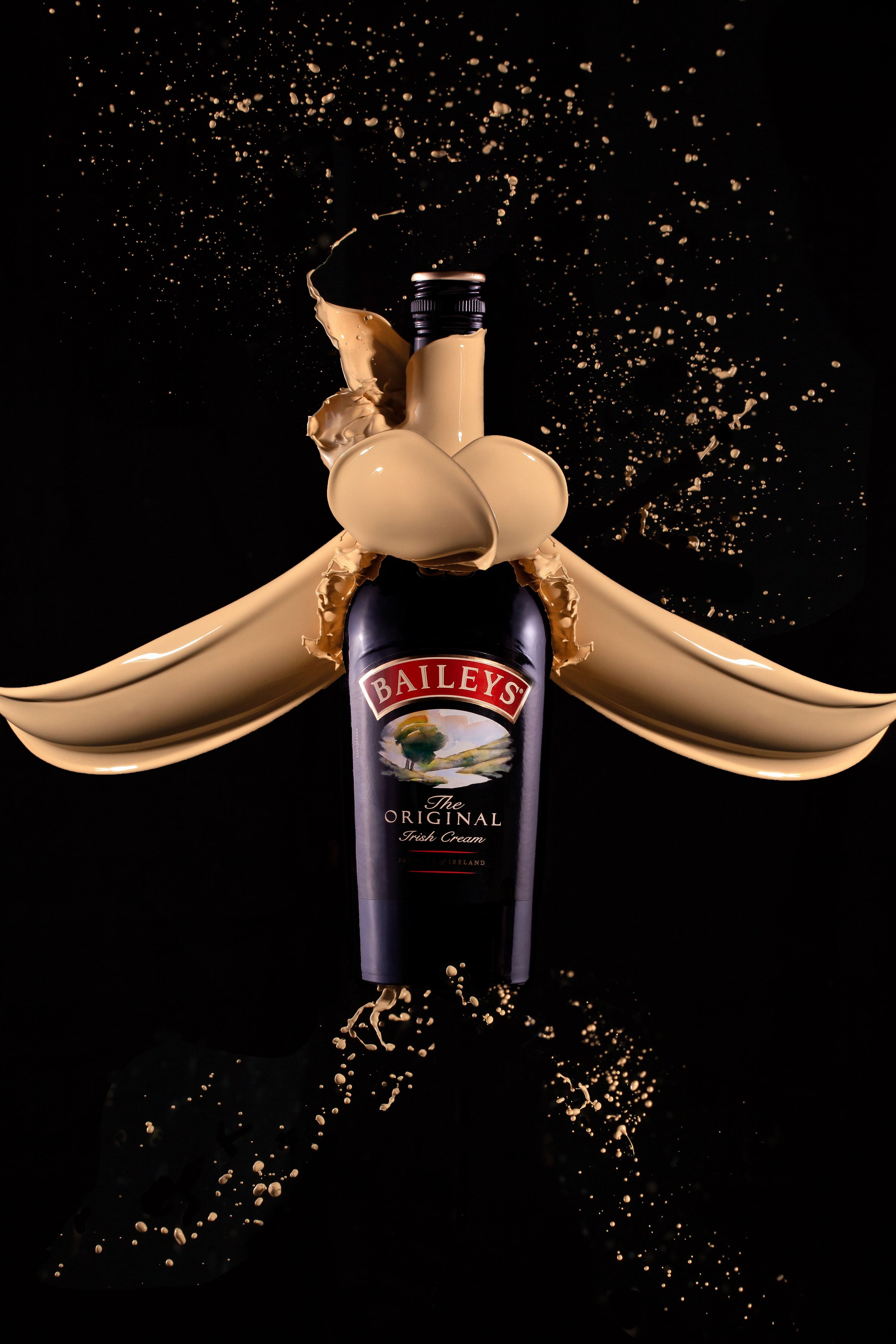 Baileys Original Irish Cream bottle with creamy beige liquid splashing around it creating a ribbon tie, against a black background