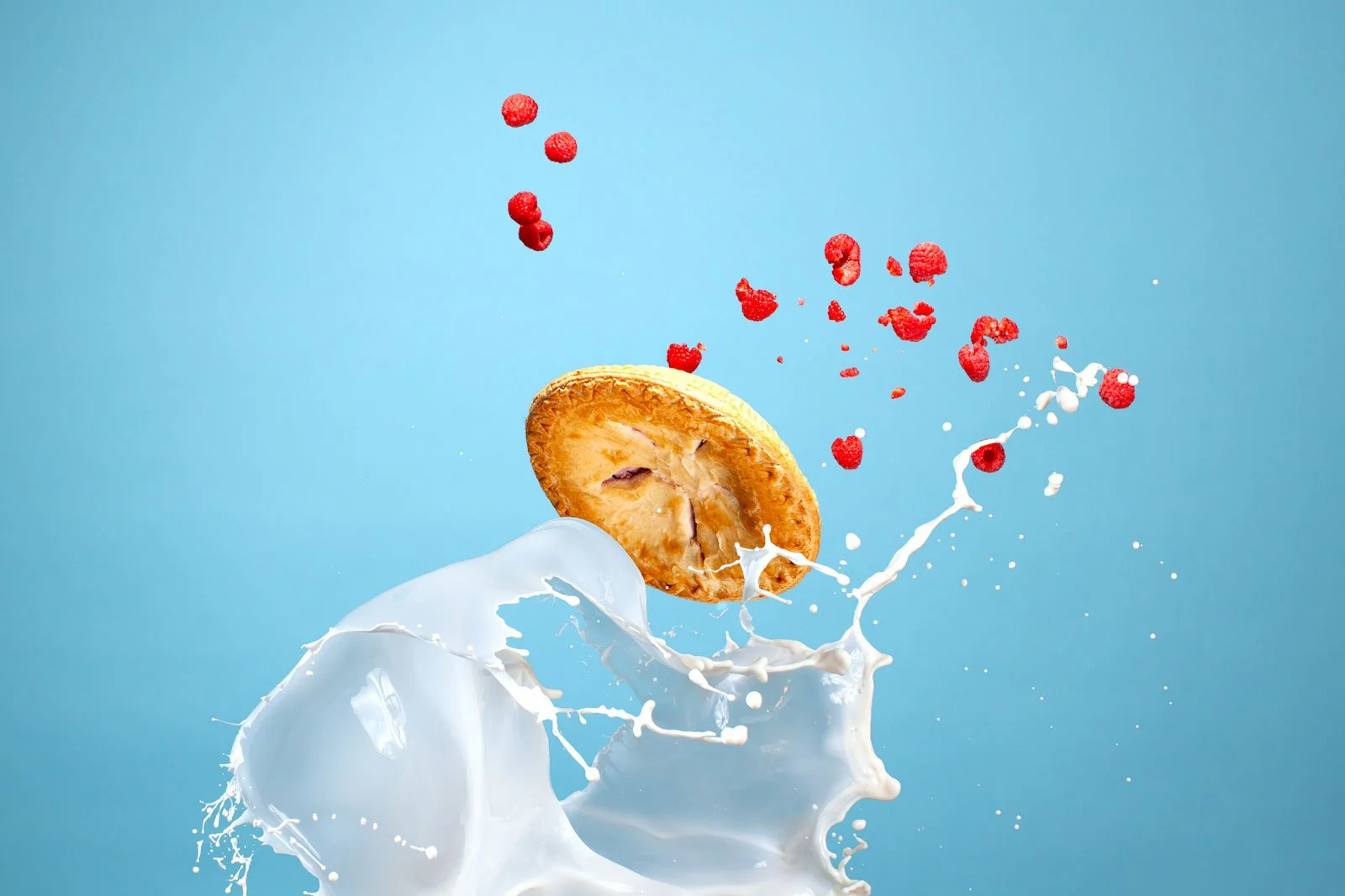 Raspberry pie splashing through milk with raspberries flying in the air against a blue background