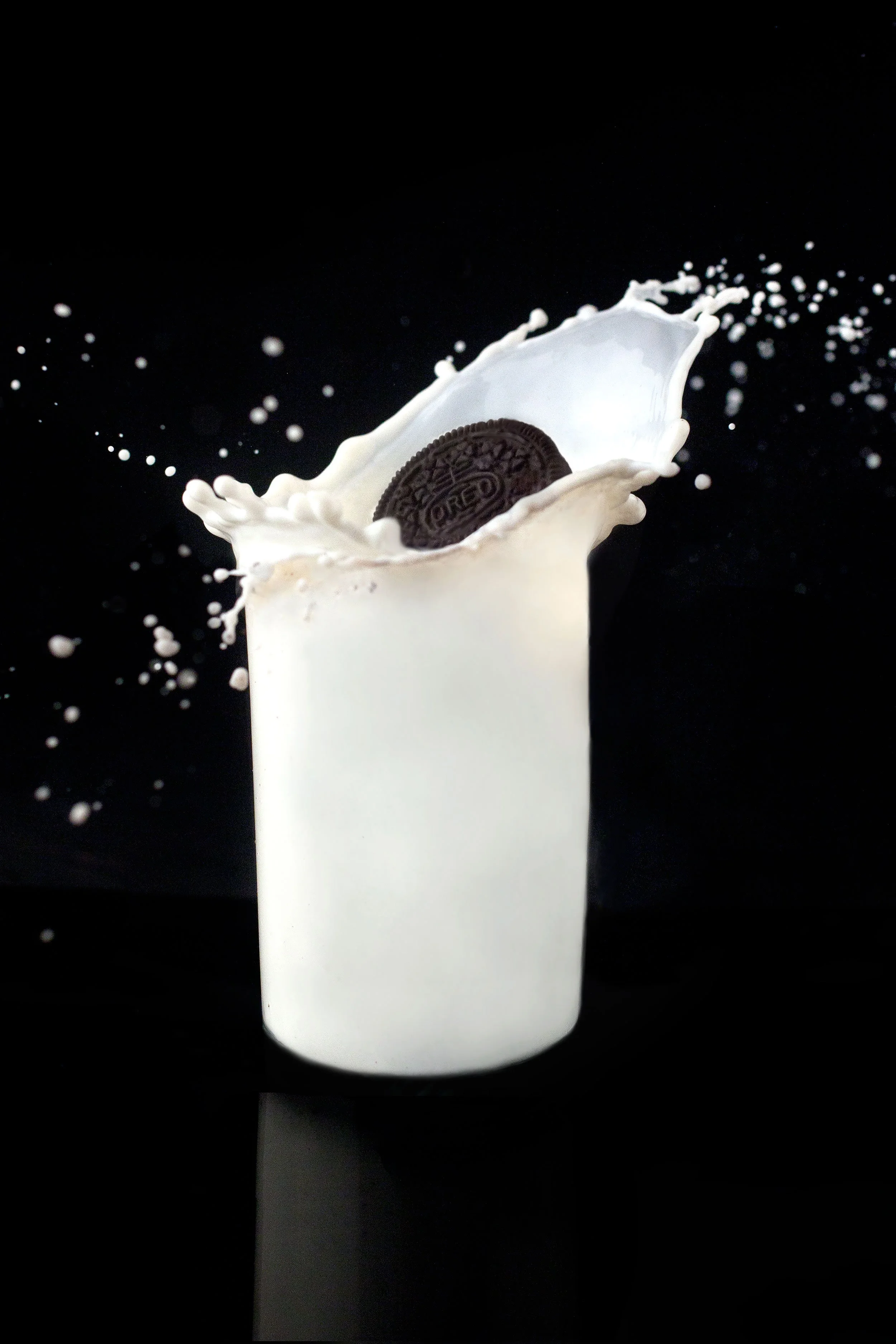 Oreo Chocolate sandwich cookie splashing into a glass of milk where the glass is no longer visible but the milk is still formed, against a black background