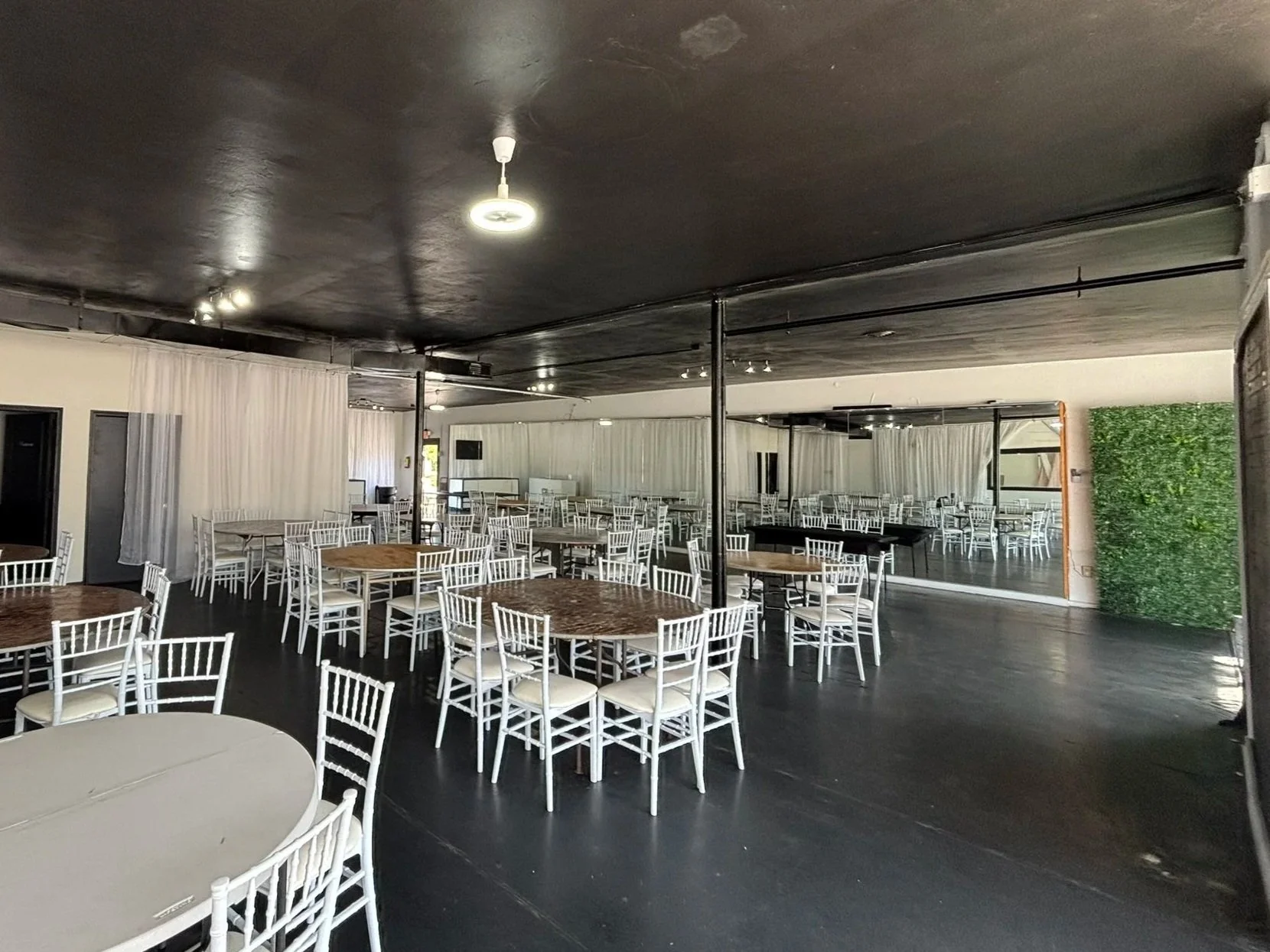 Elite banquets event hall with round tables, white chairs, dark floor, black ceiling, and a green wall on the right. essential 6hours
