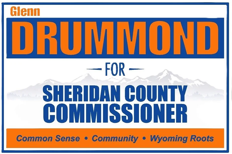 Campaign sign for Glenn Drummond, running for Sheridan County Commissioner. Features mountain background, navy blue and orange colors, and the slogan: 'Common Sense, Community, Wyoming Roots.'