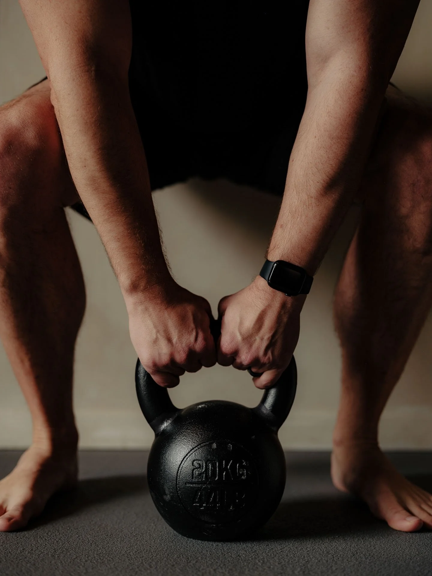 Person holding a 20 kg kettlebell with both hands in a squat position on a workout mat.