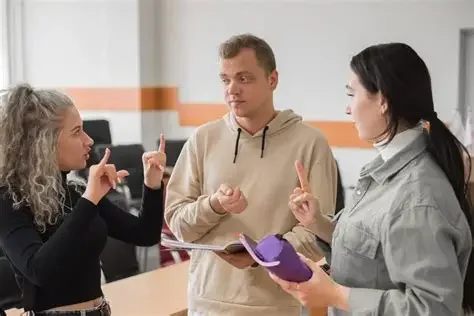 Three people, two women and one man, standing in a room having a conversation using Americal Sign Language.