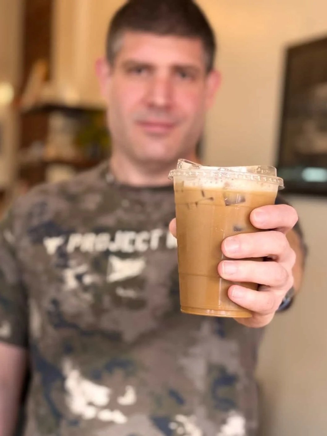 A man holding a plastic cup of iced coffee or latte, with a blurred background.