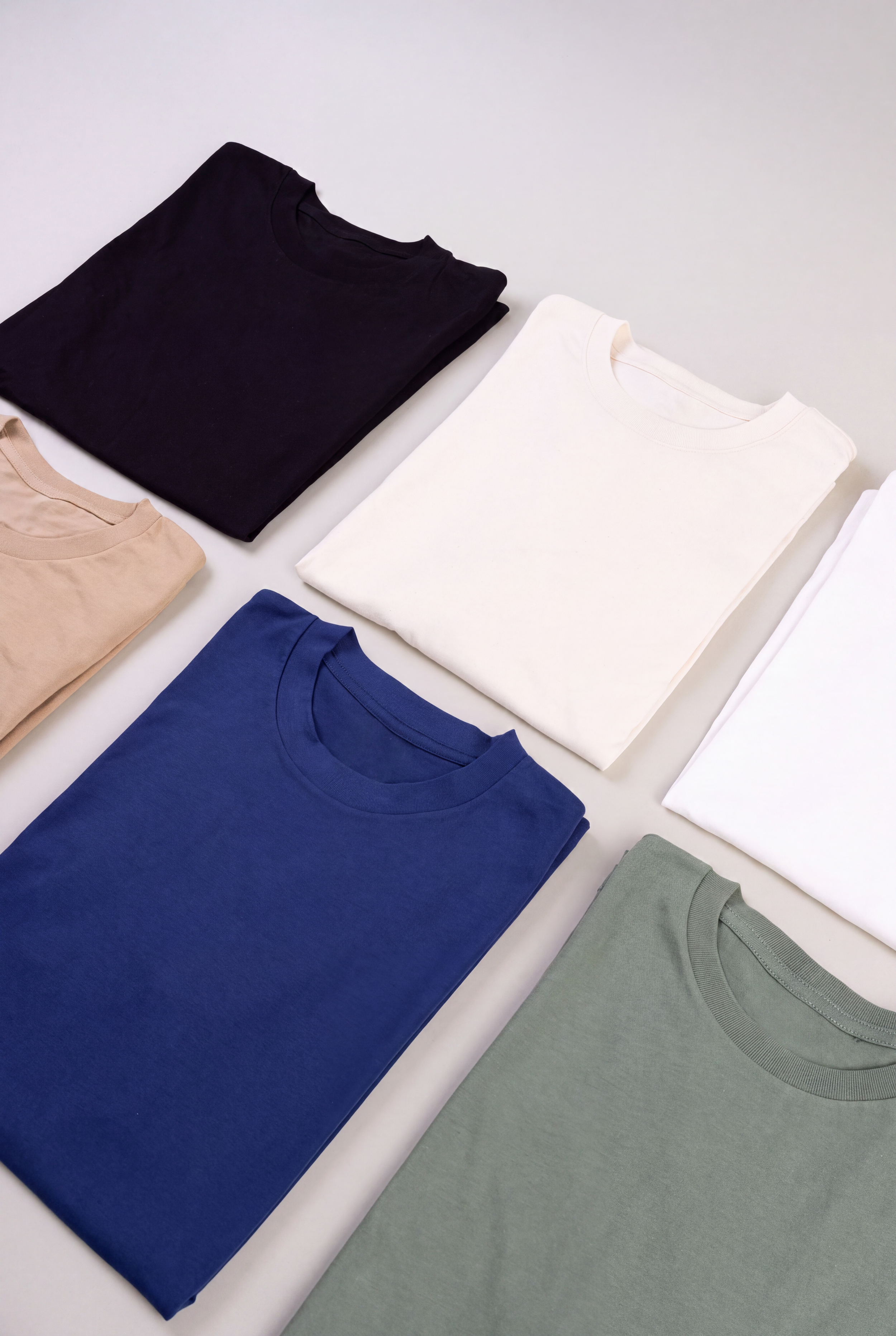 Black, beige, white, tan, navy blue, and green shirts folder neatly and placed next to each other.