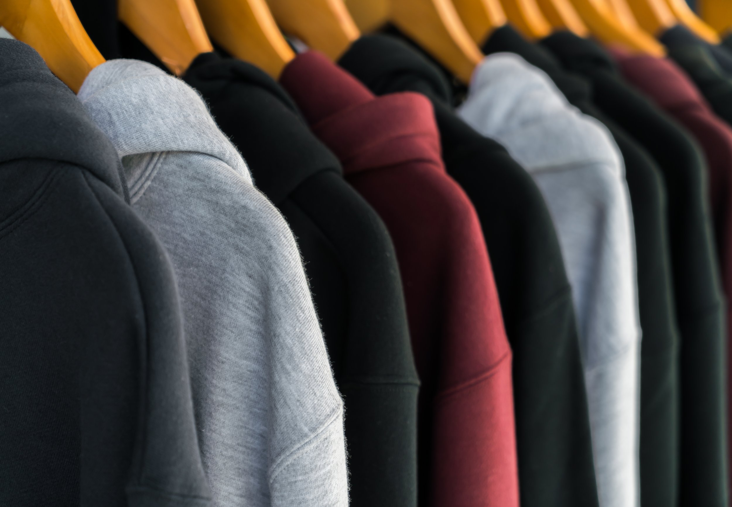 Row of hoodies hanging on wooden hangers, in colors including black, gray, burgundy, and white.