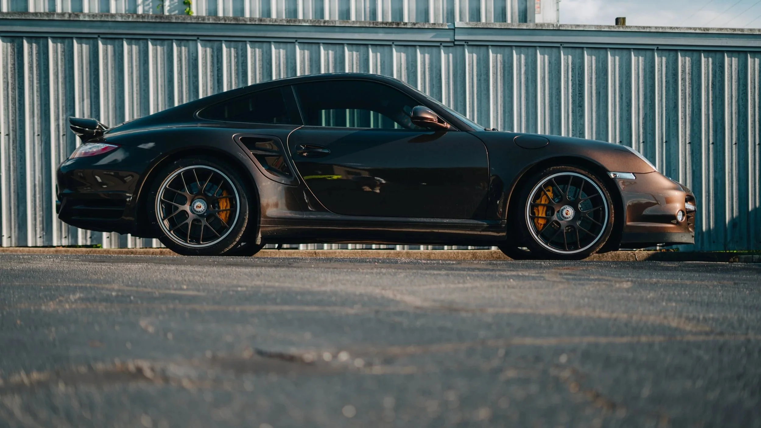 Black sports car parked on the street in front of a metal fence.