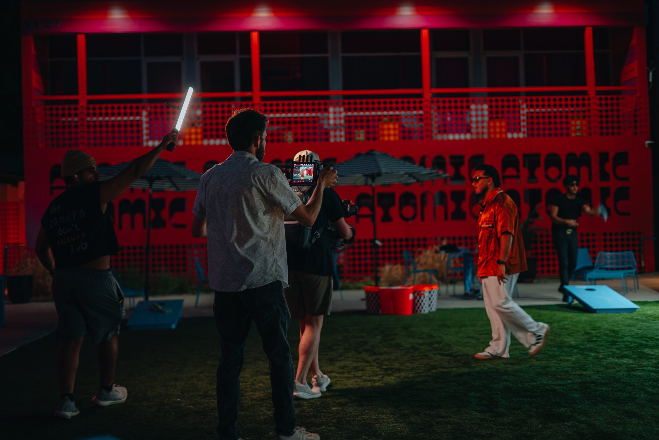 People filming and taking photos of a man practicing dance or martial arts outdoors during the evening at a social gathering or event.