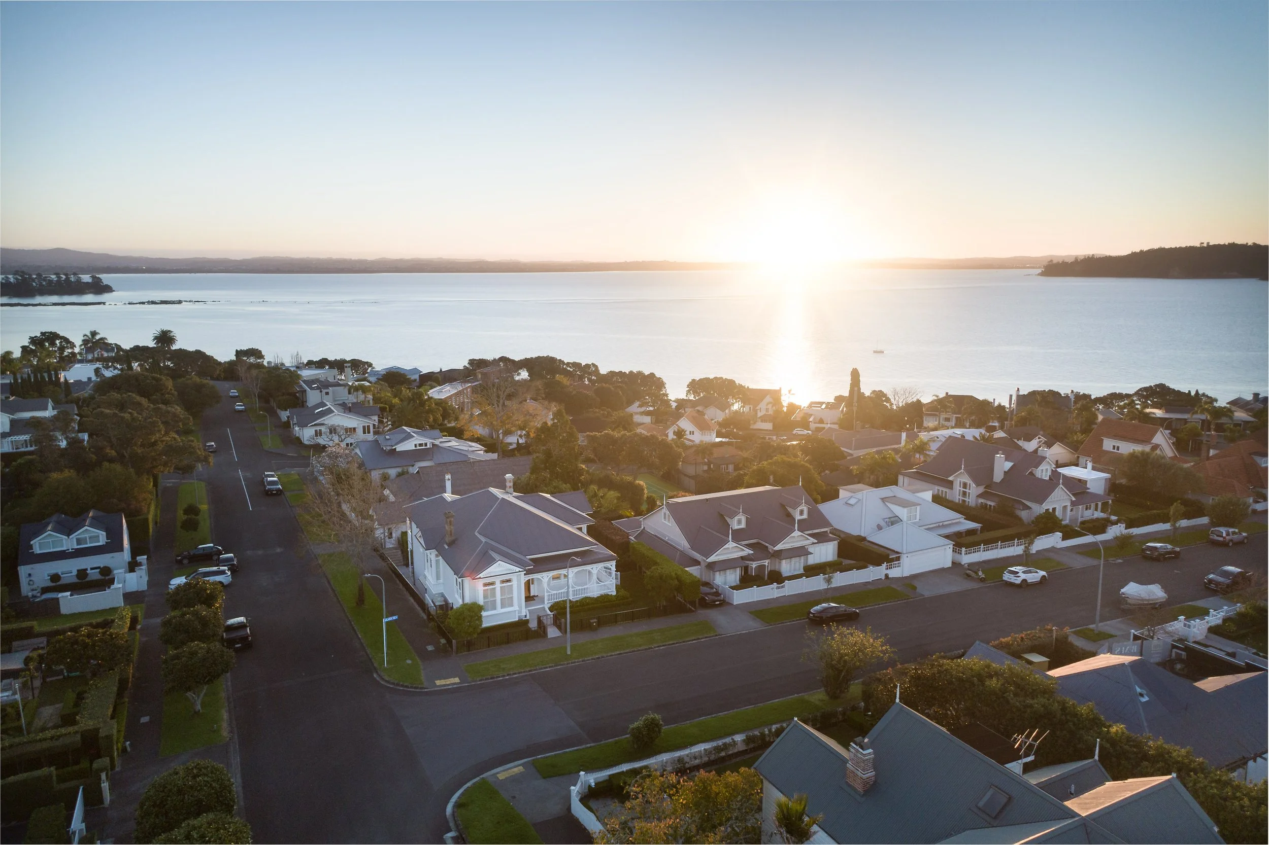 Aerial view of a residential neighborhood near a large body of water during sunset with clear blue sky.