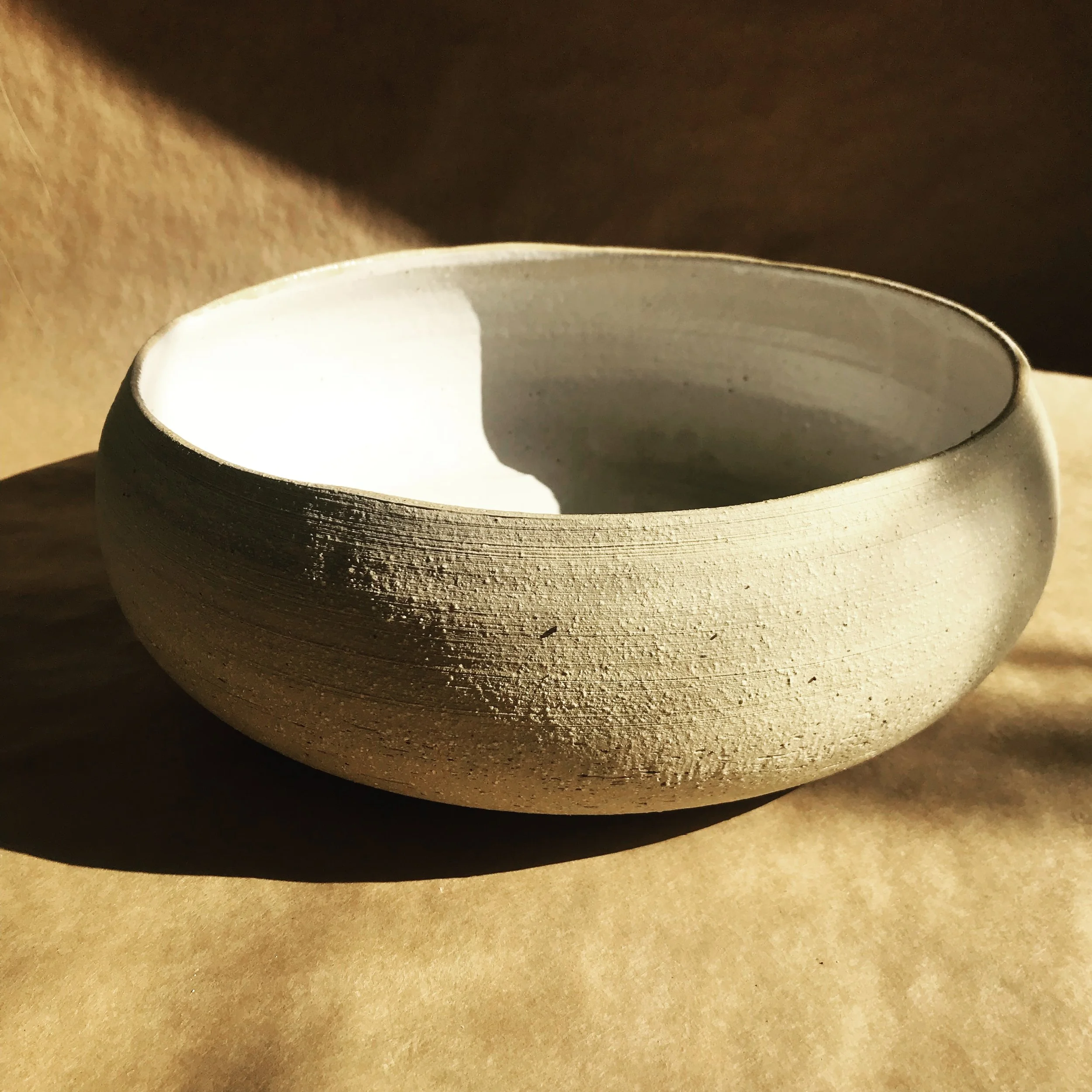 Photo of white pottery bowl with a textured natural outer surface and a white interior, placed on a brown surface.