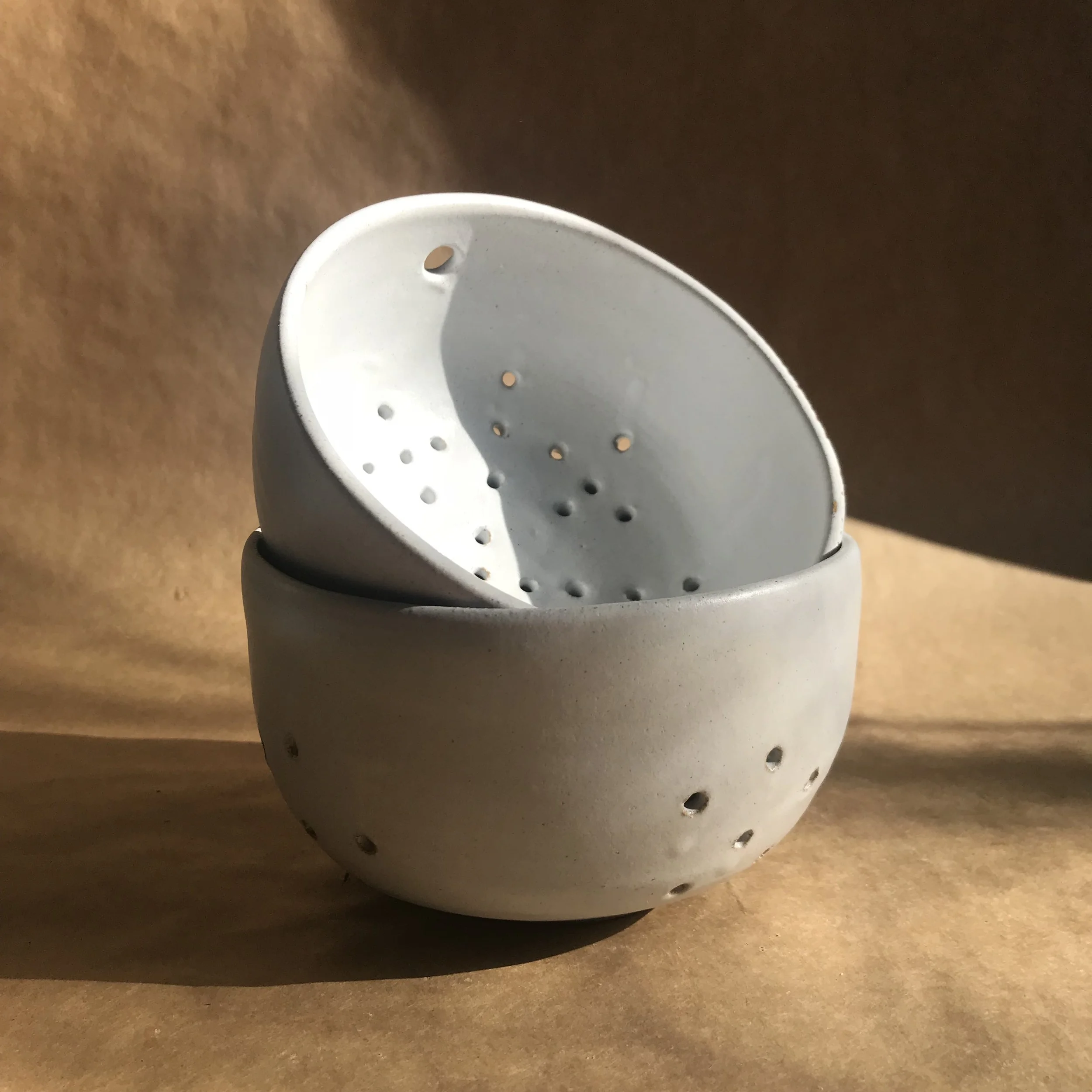 Close-up of a white, rounded handmade pottery colander or berry bowl.
