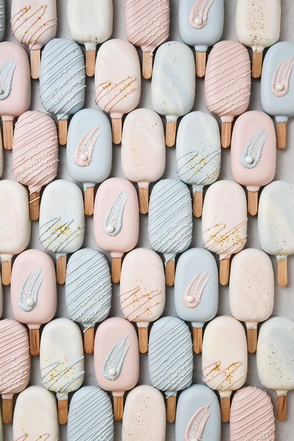 A collection of pastel-colored cakesicles arranged in a grid pattern.