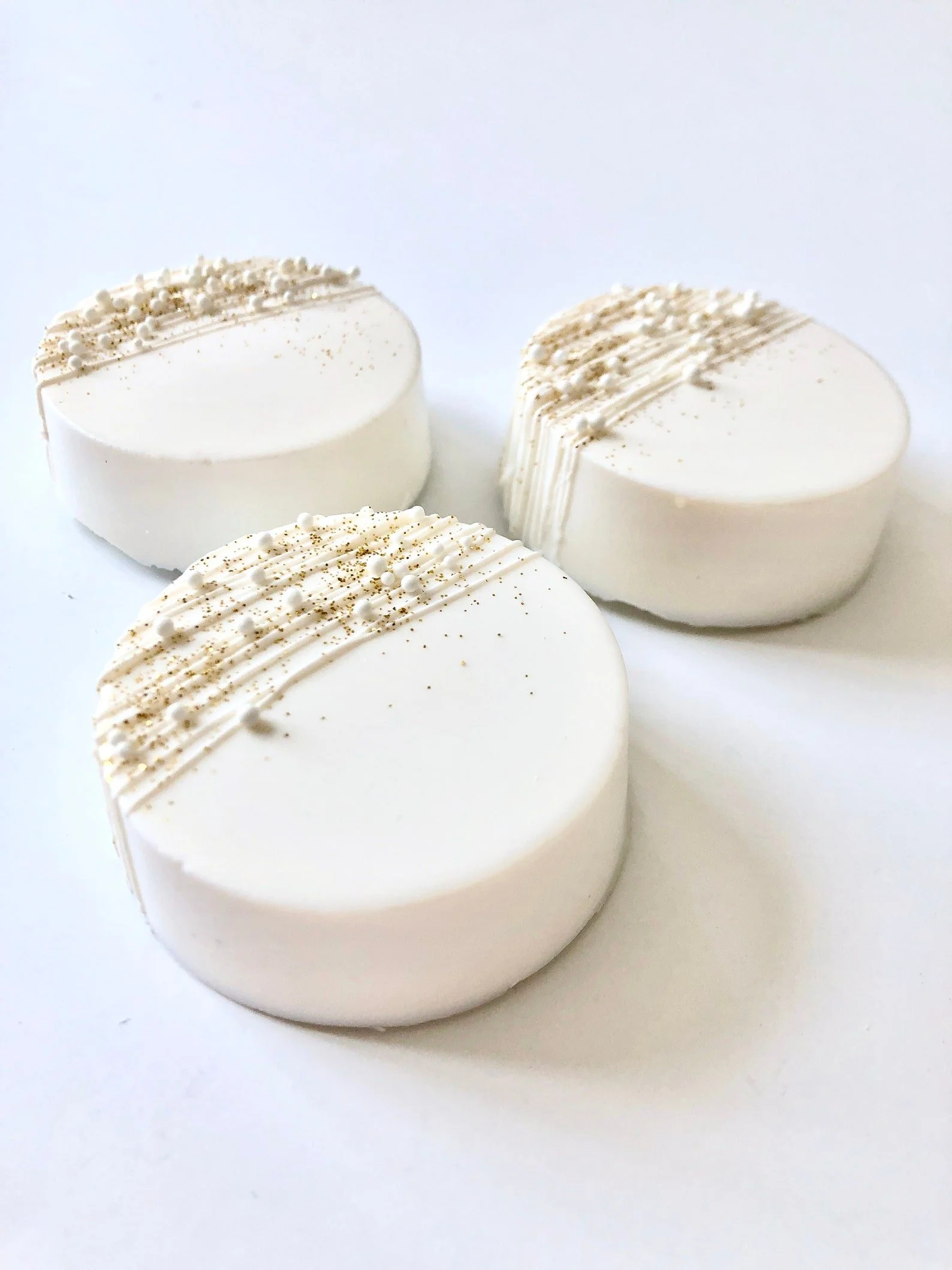Three white, round chocolate dipped Oreos with  textured decoration on top, placed on a white surface.