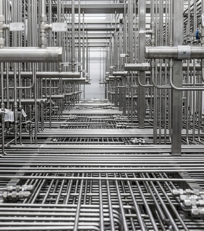 A complex network of interconnected metallic pipes in a large industrial facility or data center.