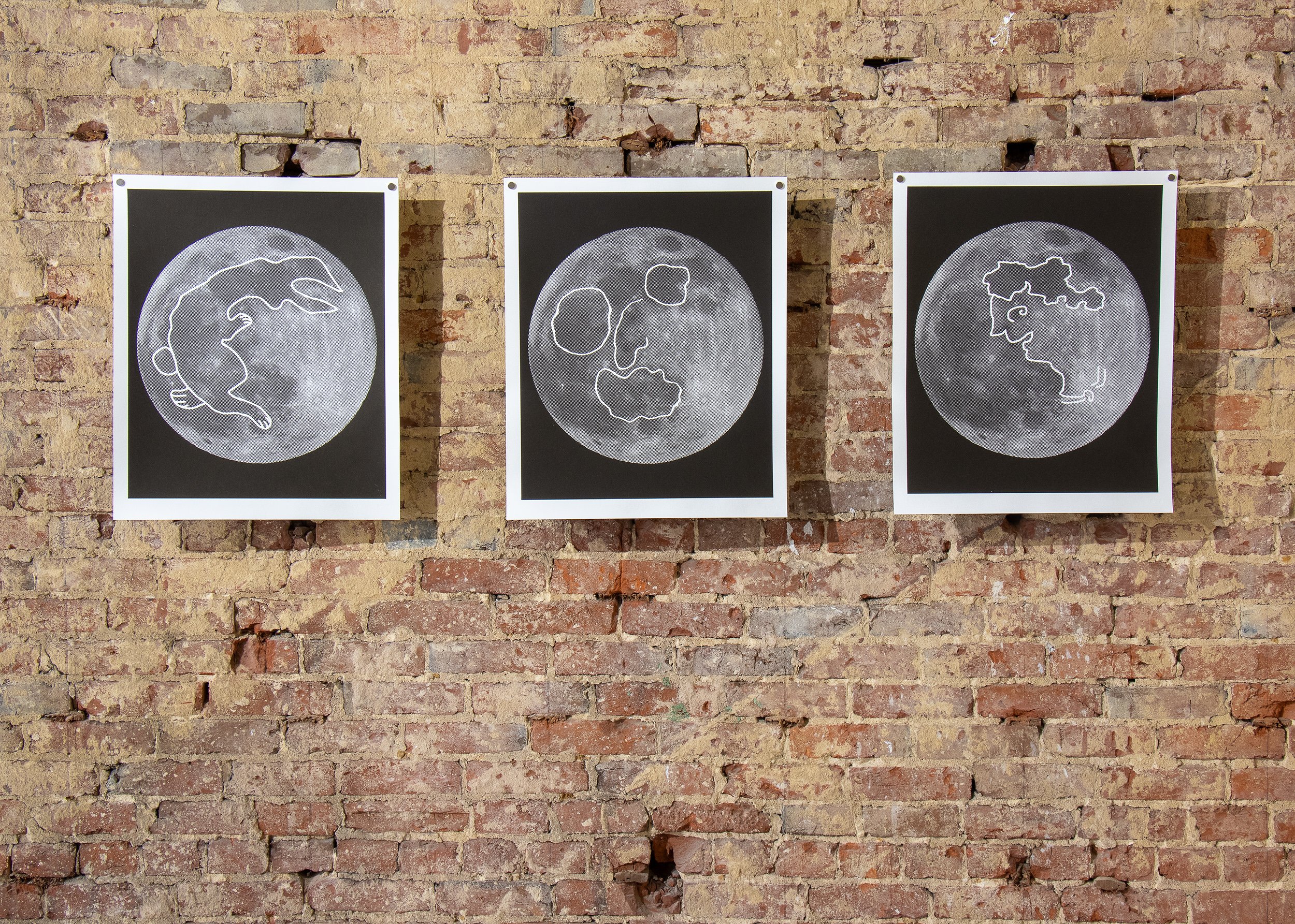 Three framed photographic artworks installed on a brick gallery wall during an exhibition.