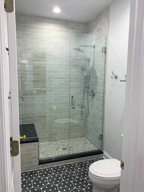 Bathroom with a glass shower enclosure, a tiled wall, and a toilet in the foreground.