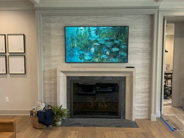 Living room with a fireplace, flat-screen TV above, basket with blanket and plant to the left, and a doorway to the right.