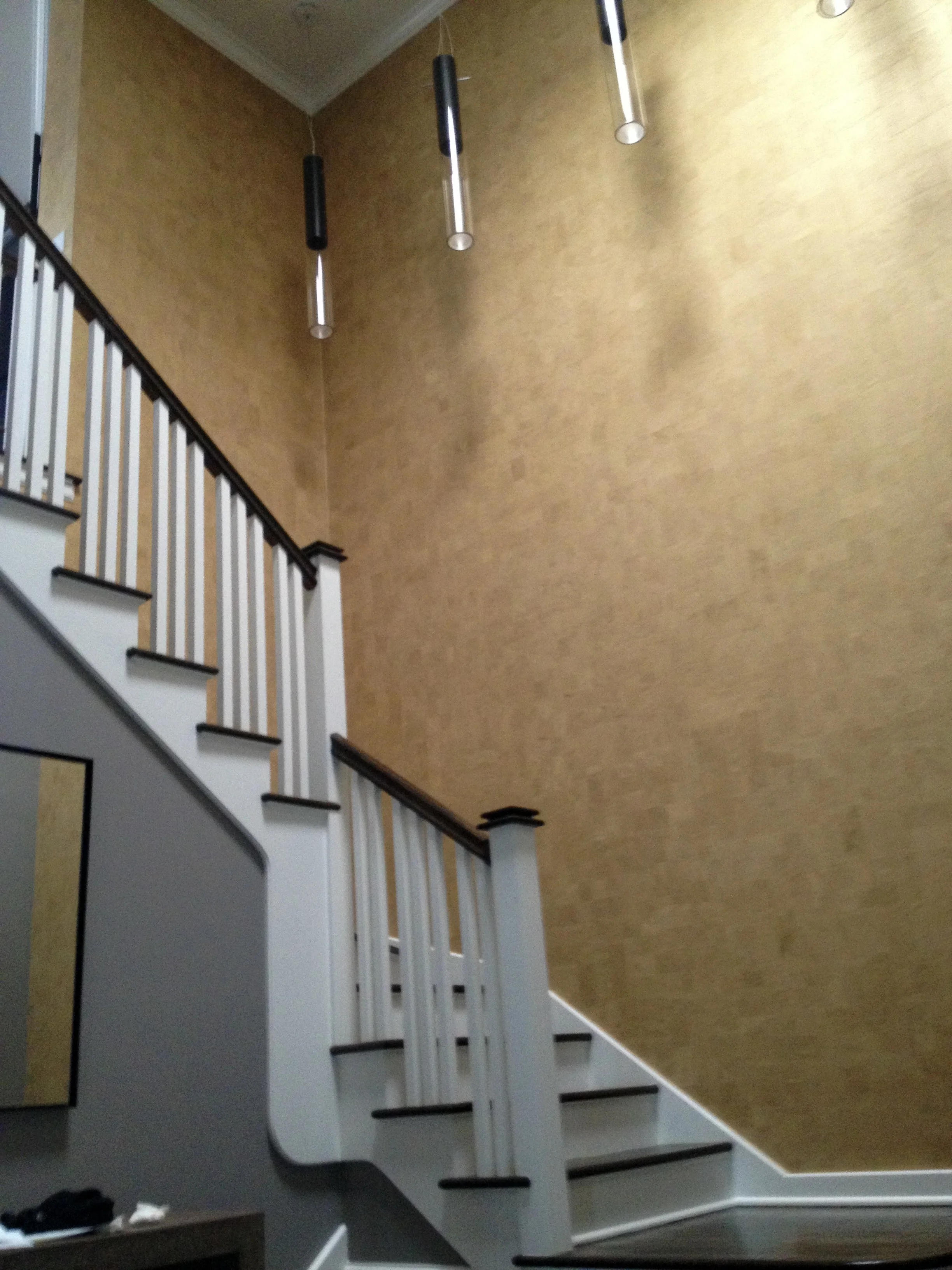 Interior of a home featuring a staircase with white railings and dark handrails, a wall painted in beige, and three hanging cylindrical pendant lights with black and white accents.