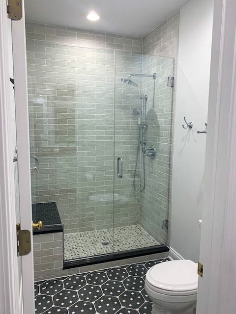 Bathroom with a glass-enclosed shower, tiled walls, black and white mosaic tile floor, and a white toilet.