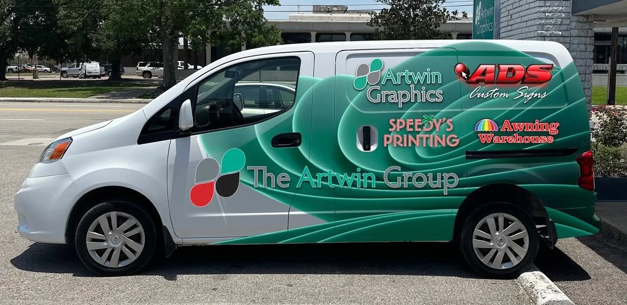 Company van with green and gray color scheme, displaying logos and names of The Artwin Group, ADS Custom Signs, Speedy's Printing, and Awning Warehouse.