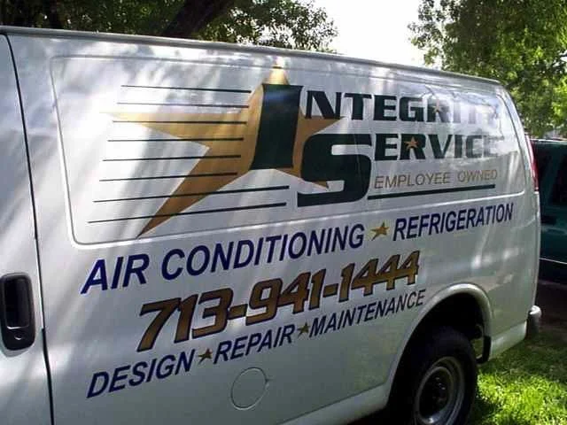 A white service van with a logo and contact information for a heating and cooling company called 'Integrity Service.' The van advertises air conditioning, refrigeration, design, repair, maintenance, and features a phone number 713-941-1444.