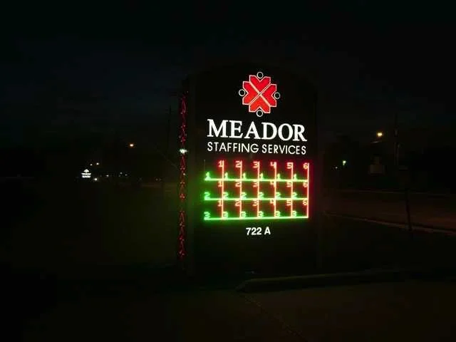 Illuminated sign for Meador Staffing Services with a red and green LED display, showing a crossword puzzle or seating chart, with the address 722 A at the bottom.