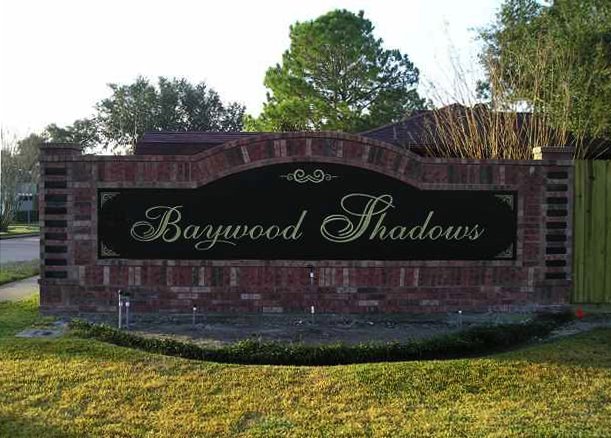 Sign for Baywood Shadows with brick border and greenery in the background.