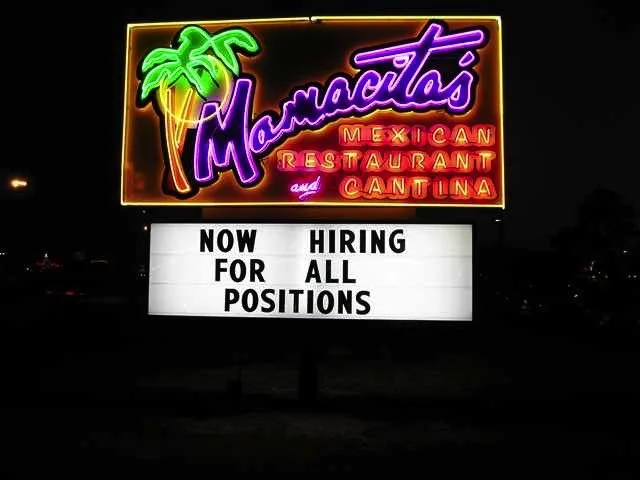 Neon sign for Mamacita's Mexican Restaurant and Cantina with palm tree graphics, and a white sign below stating 'Now Hiring All Positions'.