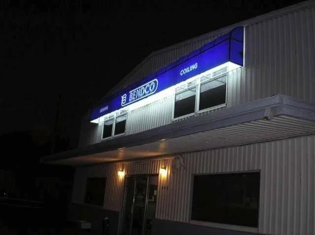 Exterior of a building at night with a blue and white sign reading 'Benaco' and 'Coiling'.